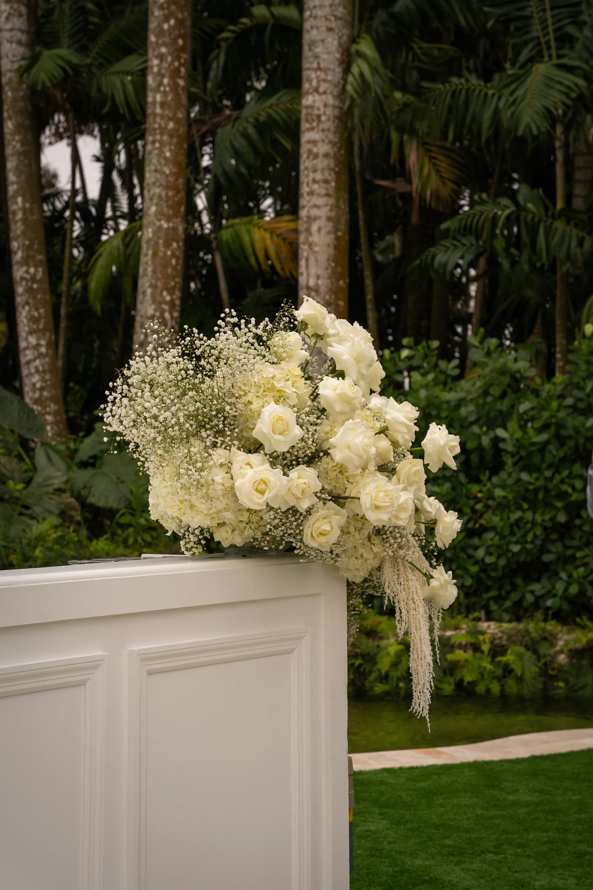 A tall white rose and gypsophila arrangement on a pedestal beside a garden path.