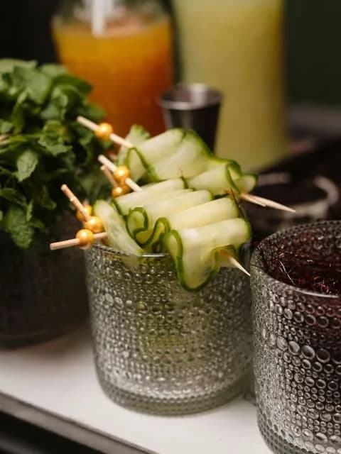 Cucumber ribbons threaded onto gold-topped picks resting on a textured green tumbler.