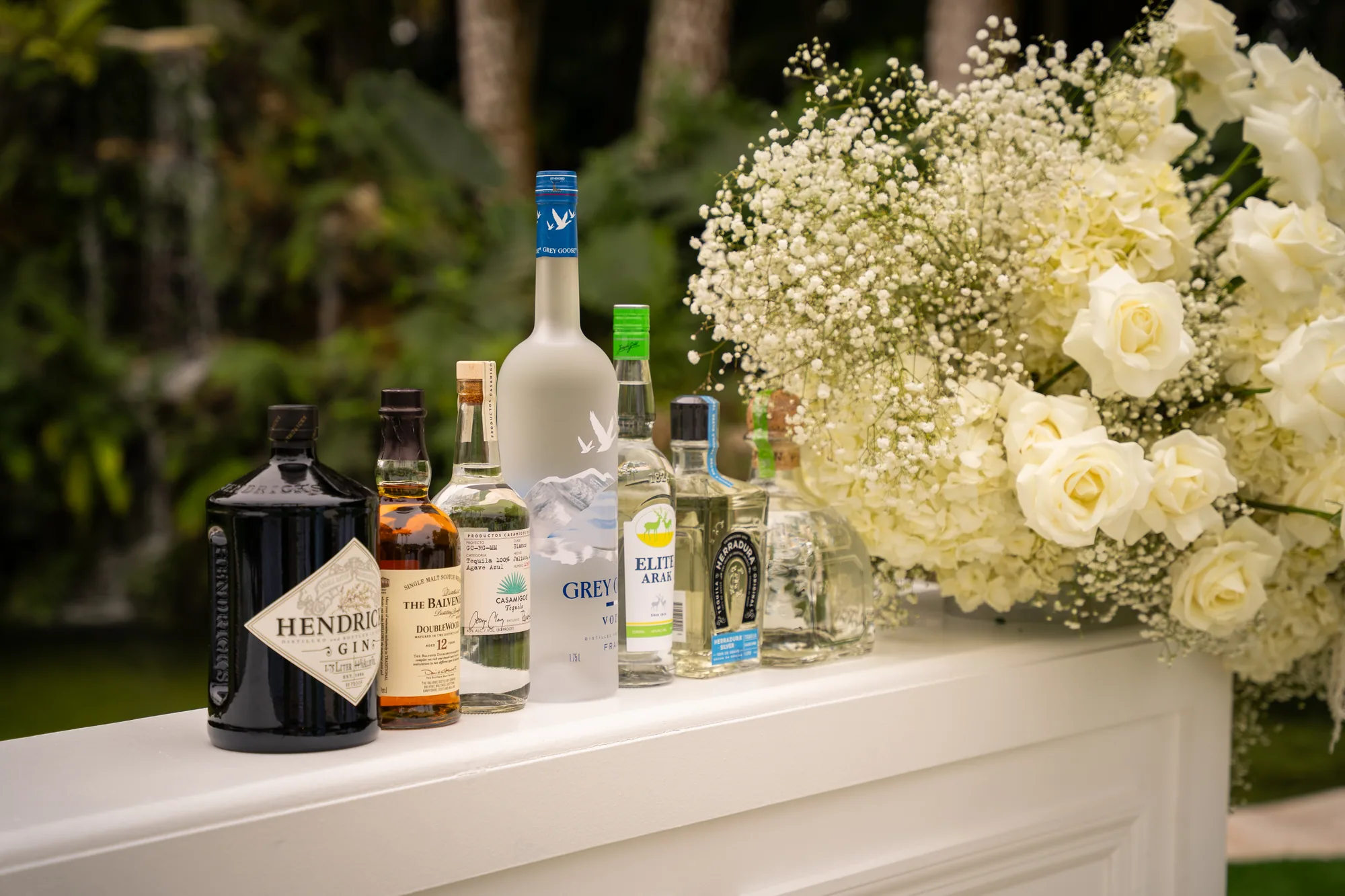 Premium spirits arranged along the bar top beside white roses and gypsophila.
